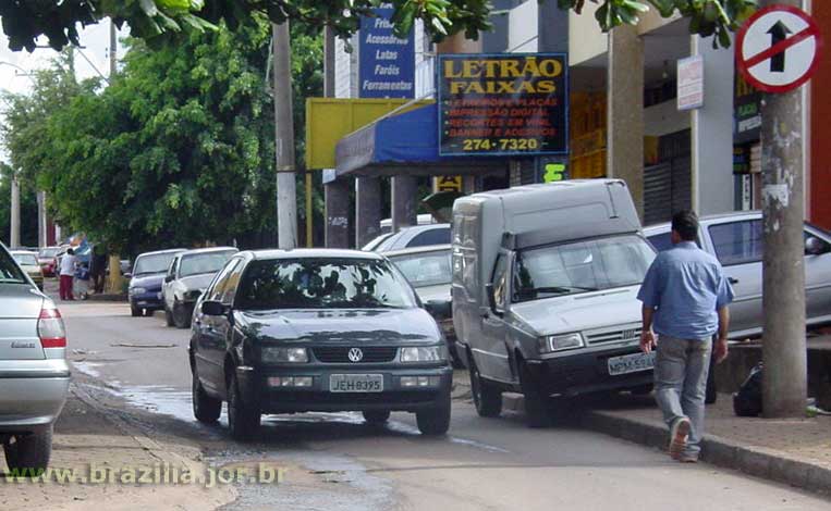 Mão única e carros estacionads sobre a calçada, na estreita via de serviço atrás dos prédios comerciais das quadras 700 norte